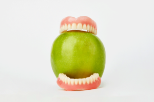 dentures clamped around green apple as example of foods to eat and foods to avoid with dentures